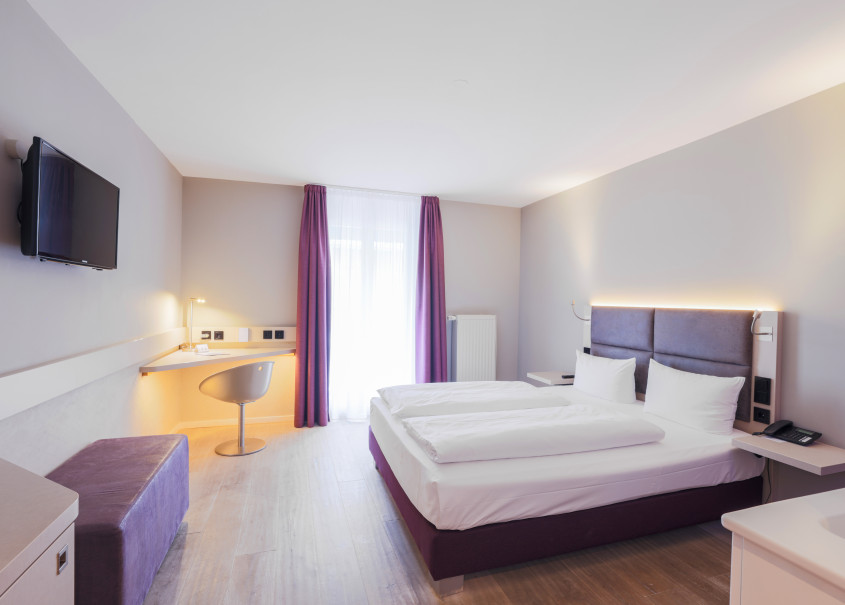 Lila Vorhänge und ein graues Doppelbett in einem Doppelzimmer des Hotel Schloss Reinach 