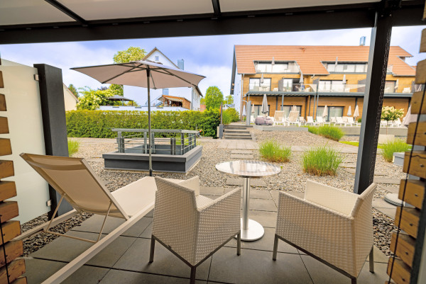 Terrasse ,it Liegestuhl, Stühlen eienem Tisch und SOnnenschirm mit Blick richtung Pool