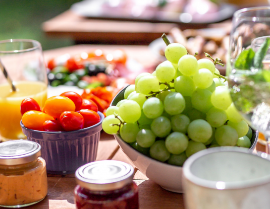 Blick auf einen Frühstückstisch mit frischem Obst und Gemüse, Orangensaft und Marmelade