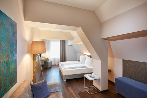 Blick ins Zimmer mit Couch, Doppelbett und würfelförmiger Sessel