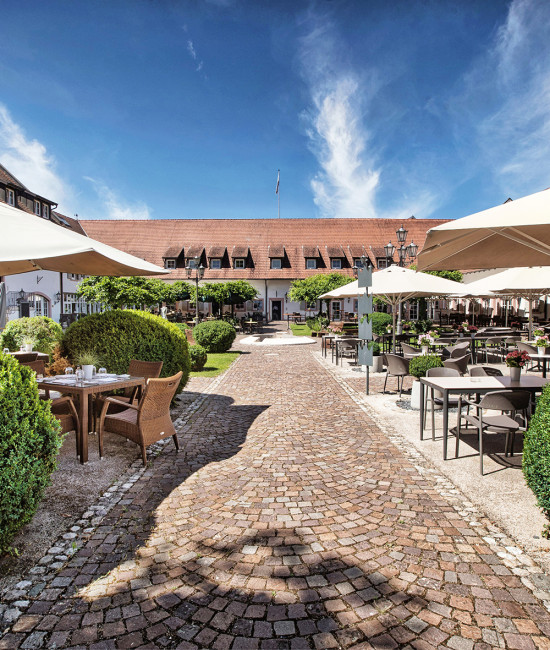 Innenhof des Hotel Schloss Reinach mit gepflstertem Weg und voielen Grünpflanzen und Sitzgelegenheiten