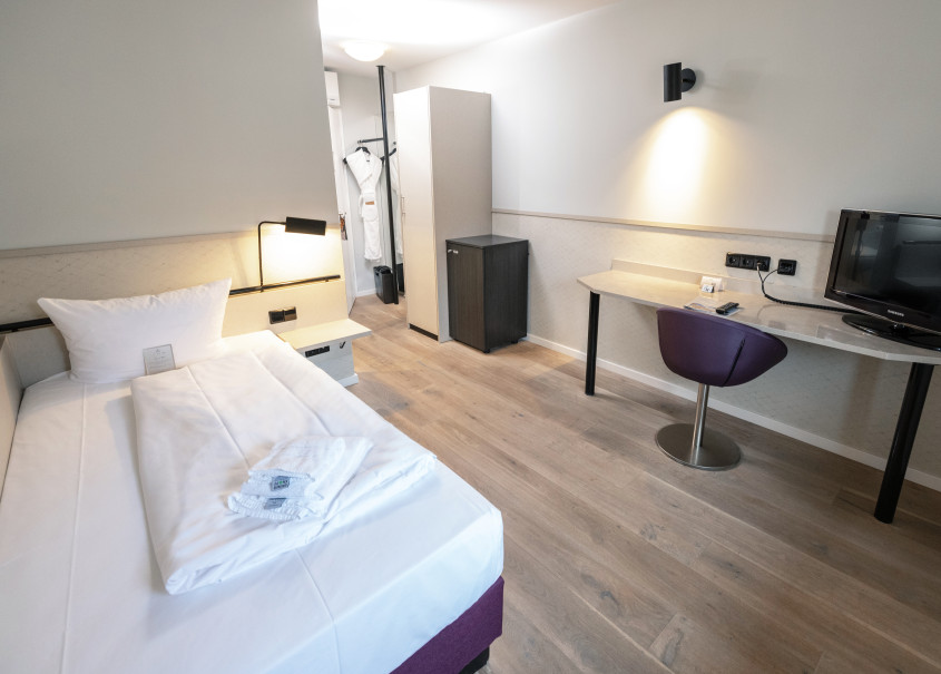 Einzelzimmer mit Kleiderschrank und Schreibtisch mit lila Stuhl 