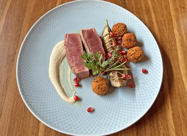 Lammrücken mit Aubergine und Falafel auf einem hellblauen Teller angerichtet
