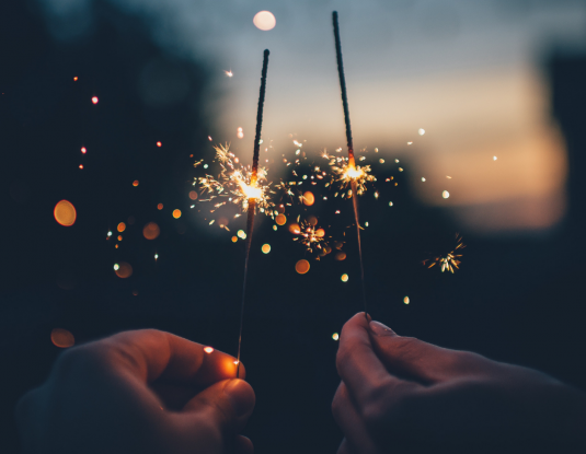 Zwei Hände halten zwei funkelnde Wunderkerzen in der Nacht 