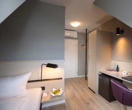 Modernes Einzelzimmer in Grautönen mit weißem Bett und lila Stuhl
