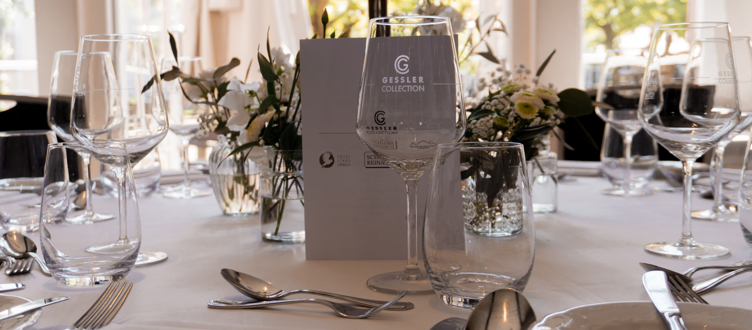 Festlich gedeckter Tisch mit weißer Tischdecke, Menükarte, Blumenarrangements